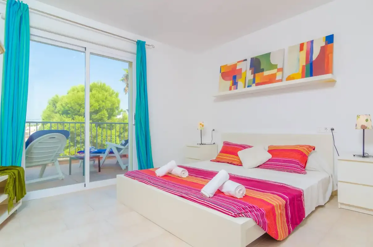 A bright bedroom with a colorful bedspread and sliding glass doors opening to a balcony.