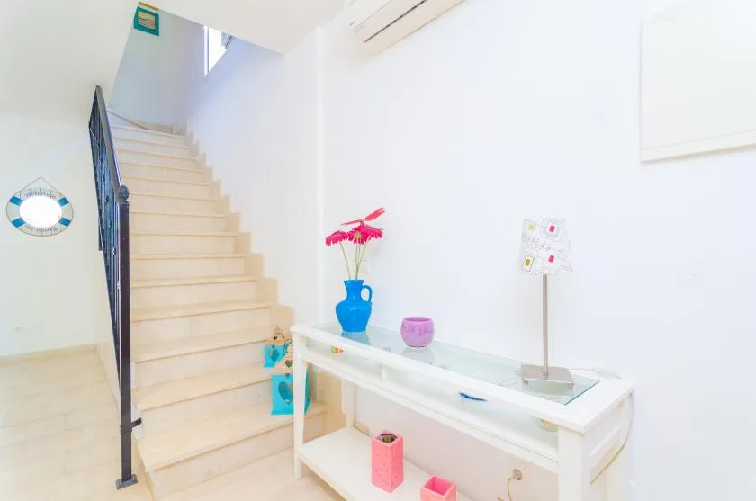 A bright interior staircase rises beside a white console table with decorative items.