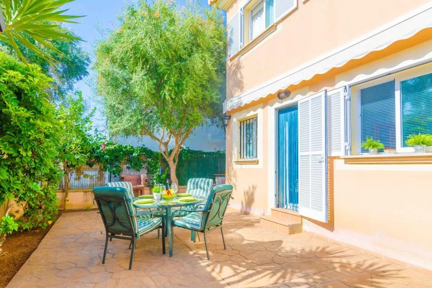 A sunny patio with outdoor seating beside a house and leafy trees.
