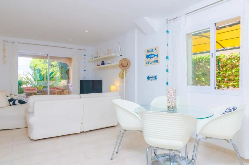A bright living and dining area with white seating and a glass-top table.