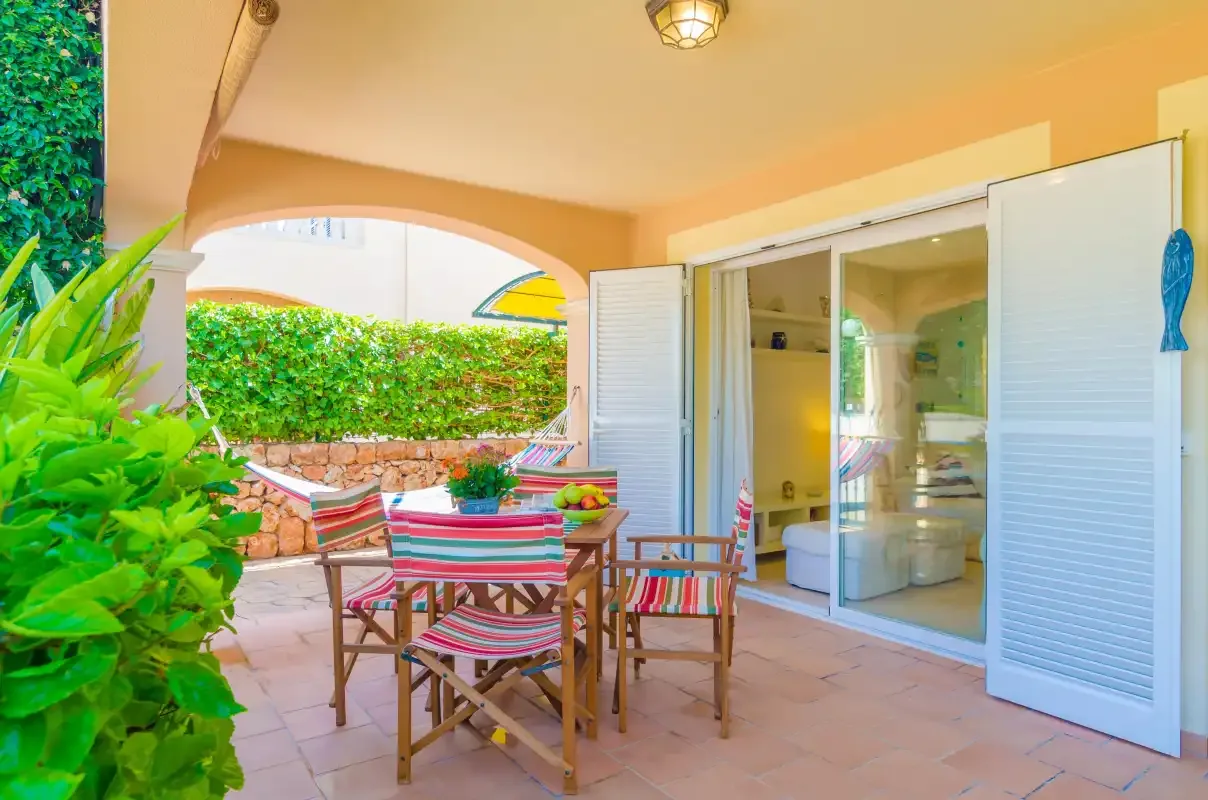 A shaded patio with a dining table and chairs beside open glass doors.
