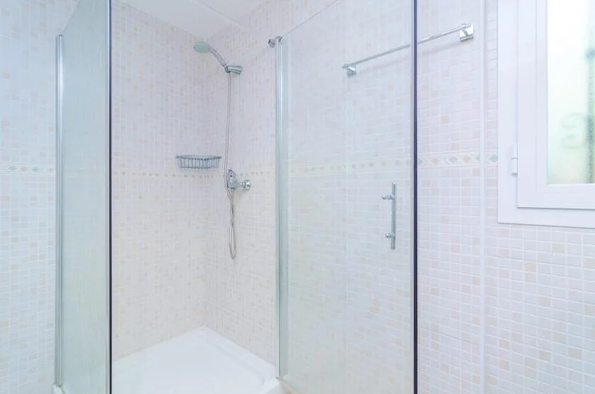 A tiled bathroom with a glass shower and a small window.