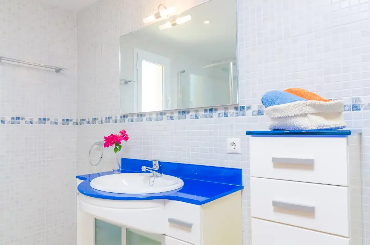 A bright bathroom with a blue countertop, sink, and large wall mirror.