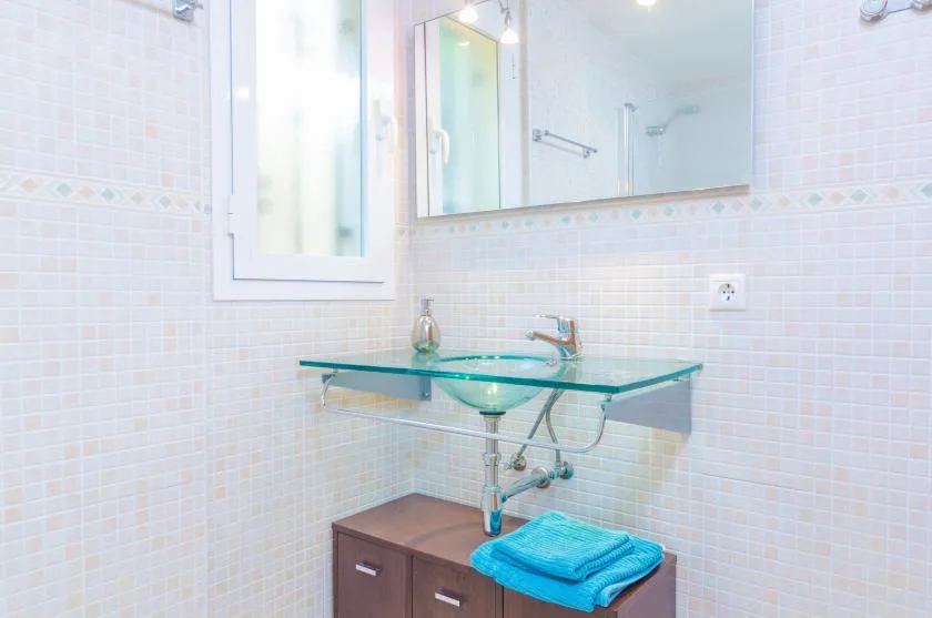 A bright tiled bathroom has a glass sink and a large wall mirror.