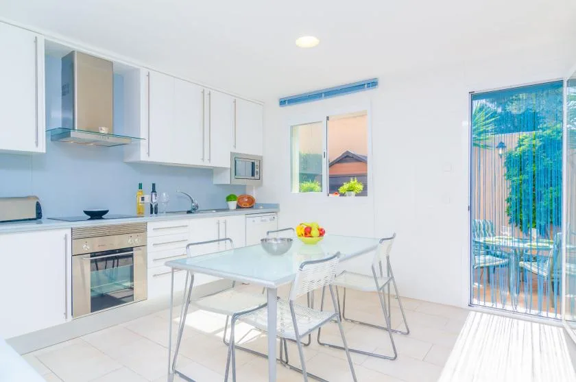 A bright kitchen and dining area with white cabinets and a glass-topped table.