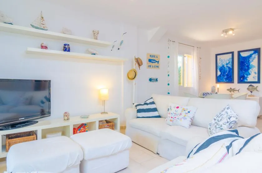 A bright living room with white seating, a television, and blue ocean-themed artwork.