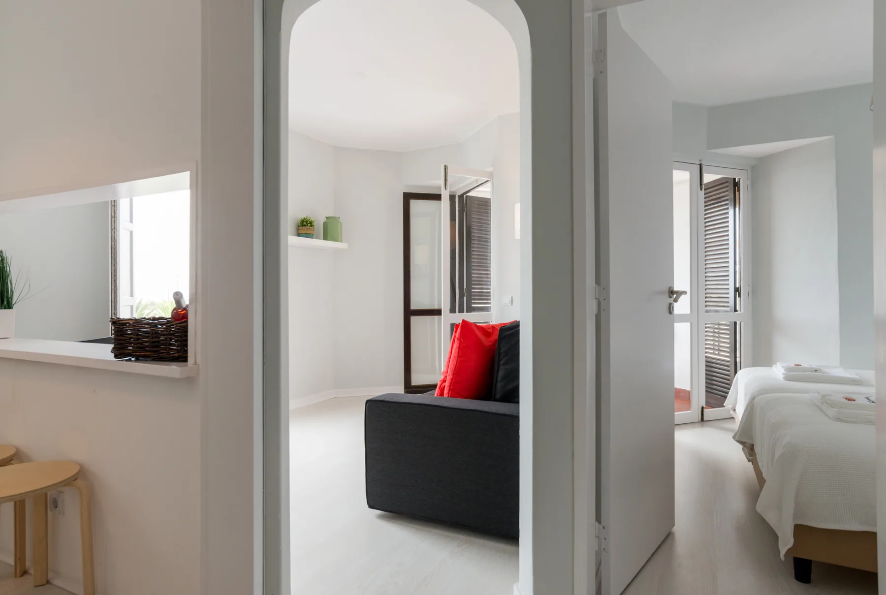 A bright apartment interior with a dark sofa and a bedroom visible through the doorway.