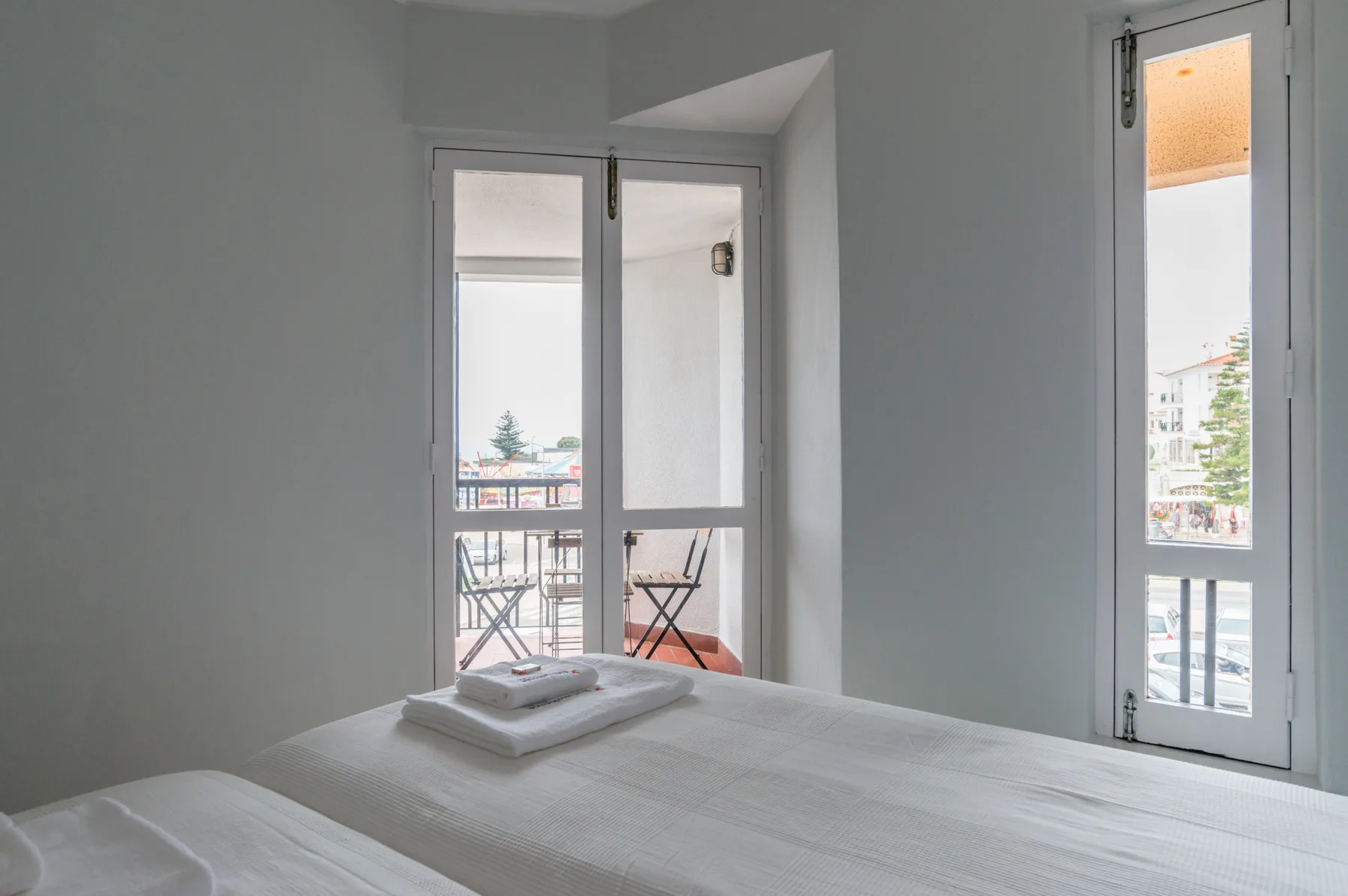 A bedroom with a neatly made bed and windows opening onto a balcony.