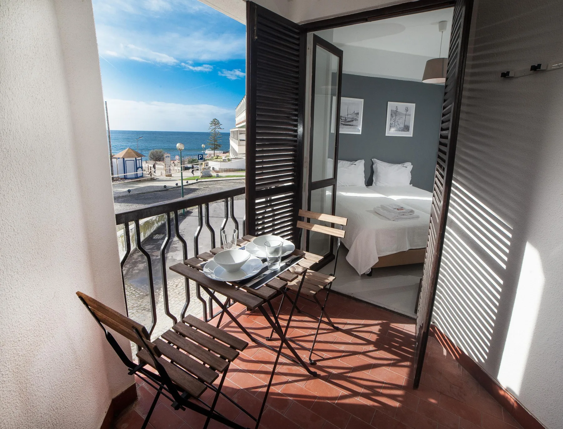 A small balcony with seating overlooks the ocean beside an open bedroom.