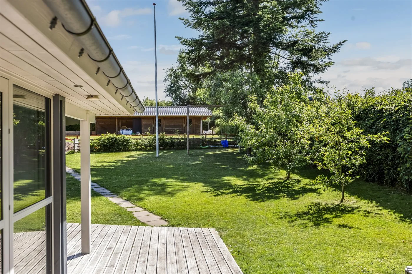 Una plataforma de madera da a un jardín con césped, árboles y arbustos.