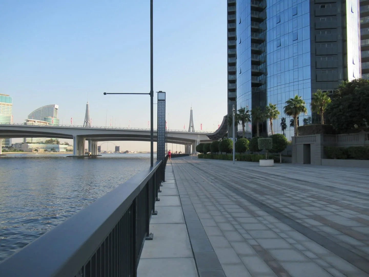 Un paseo pavimentado junto al río pasa junto a edificios modernos.