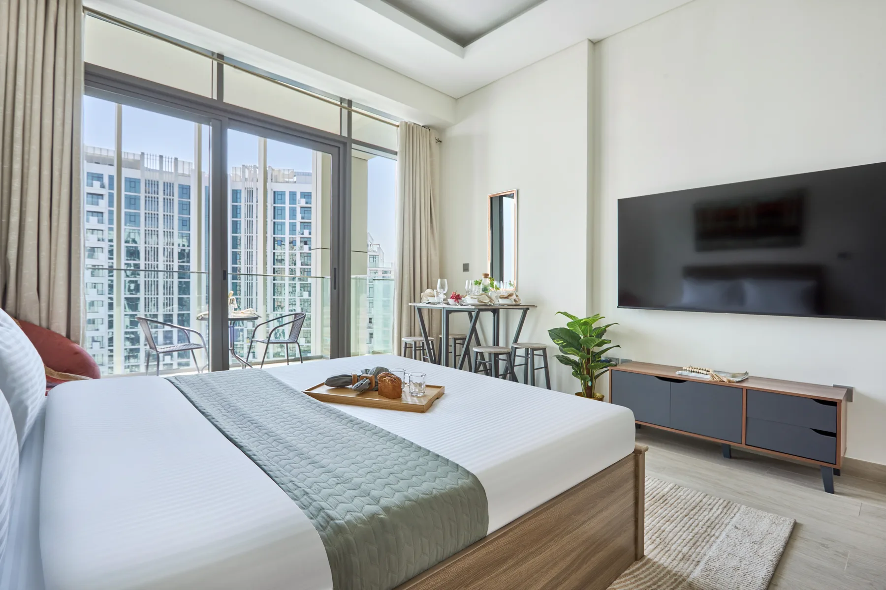 Un dormitorio luminoso con una cama, grandes ventanas y un televisor.