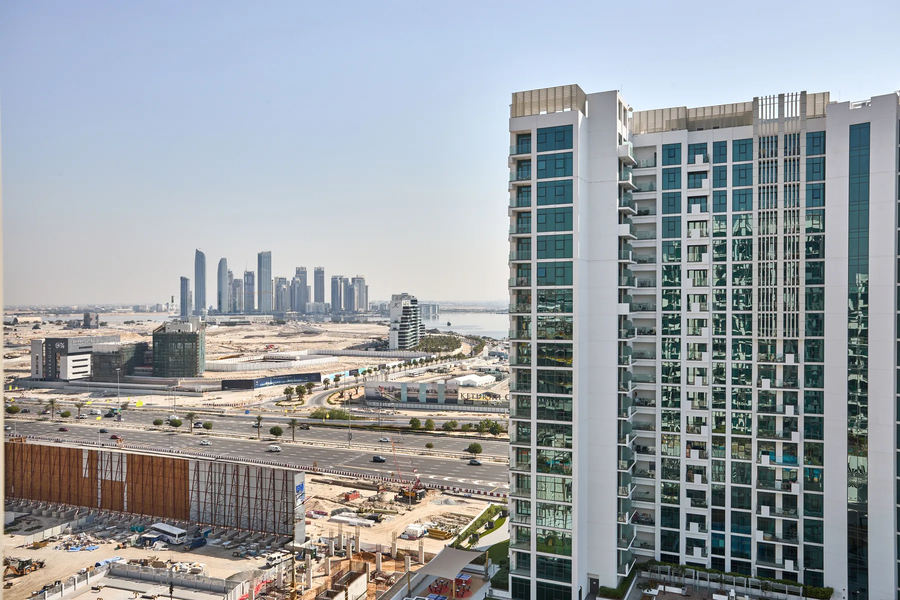 Un edificio alto domina carreteras, obras de construcción y un grupo de torres a lo lejos.