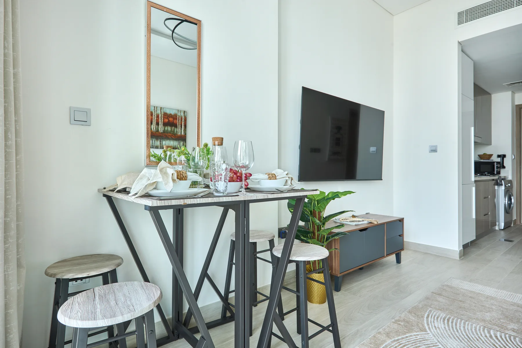 Comedor con una mesa puesta, taburetes y un televisor instalado en la pared.