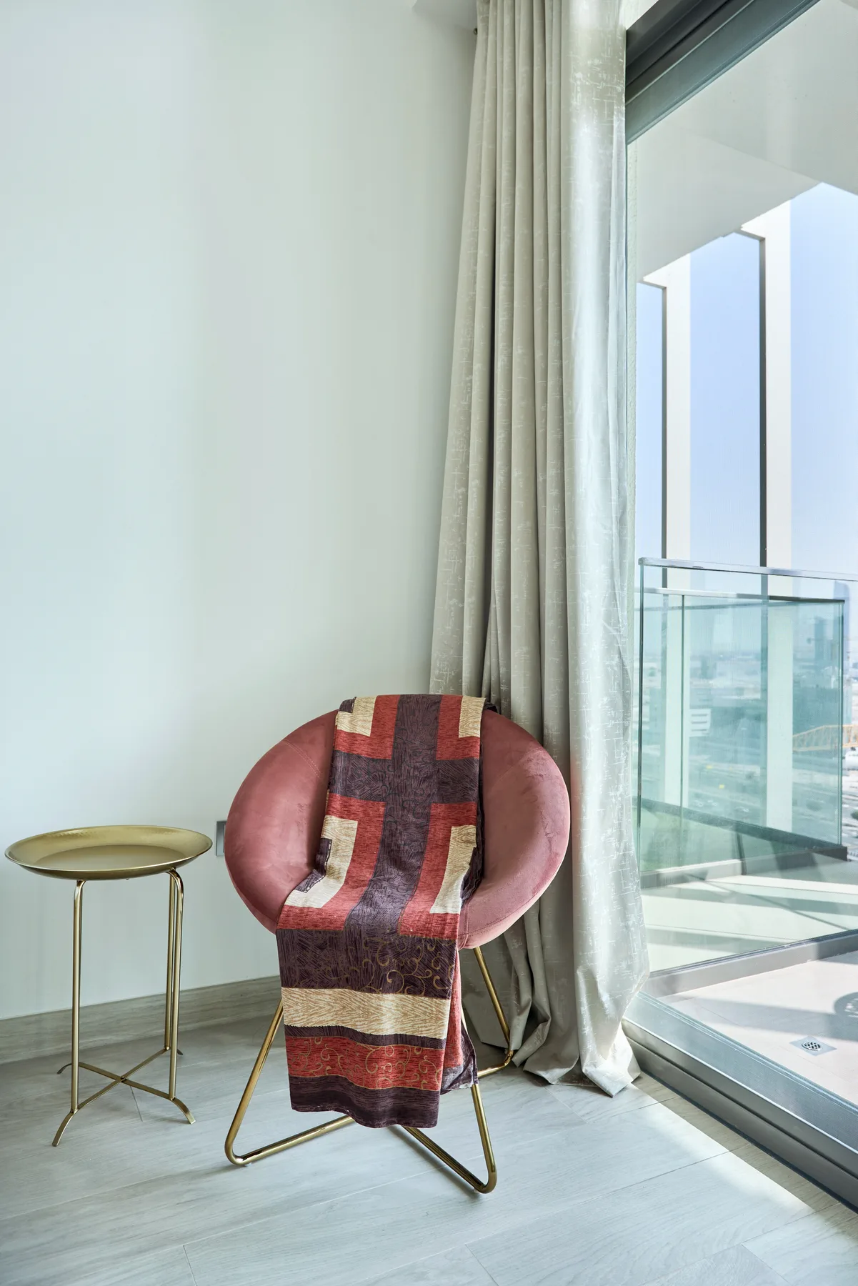 Un sillón rosa con una manta estampada está junto a una ventana de suelo a techo.