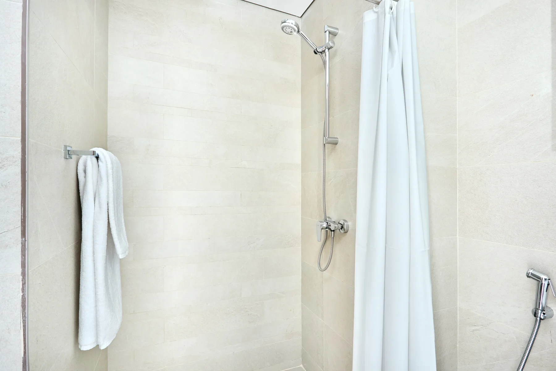 Una ducha de baño alicatada con cortina colgante y toallas en un soporte de pared.