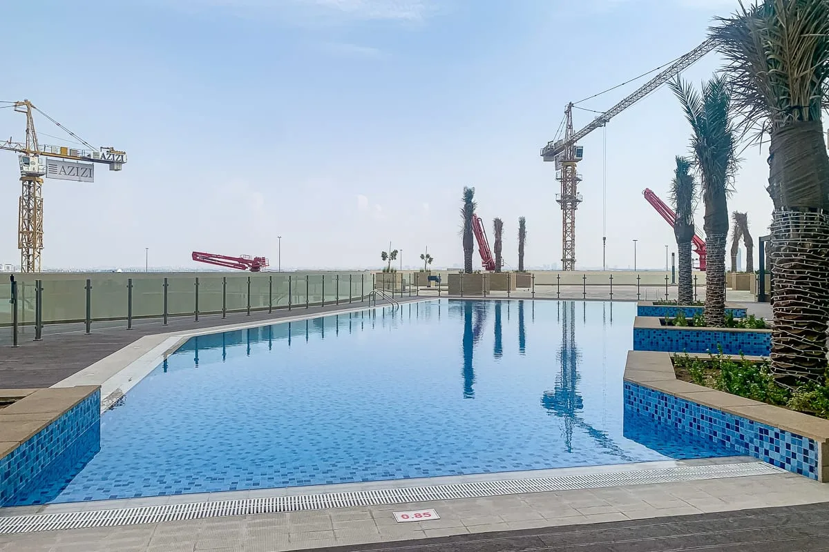 Una piscina al aire libre da a una obra, con grúas visibles al otro lado de la valla.
