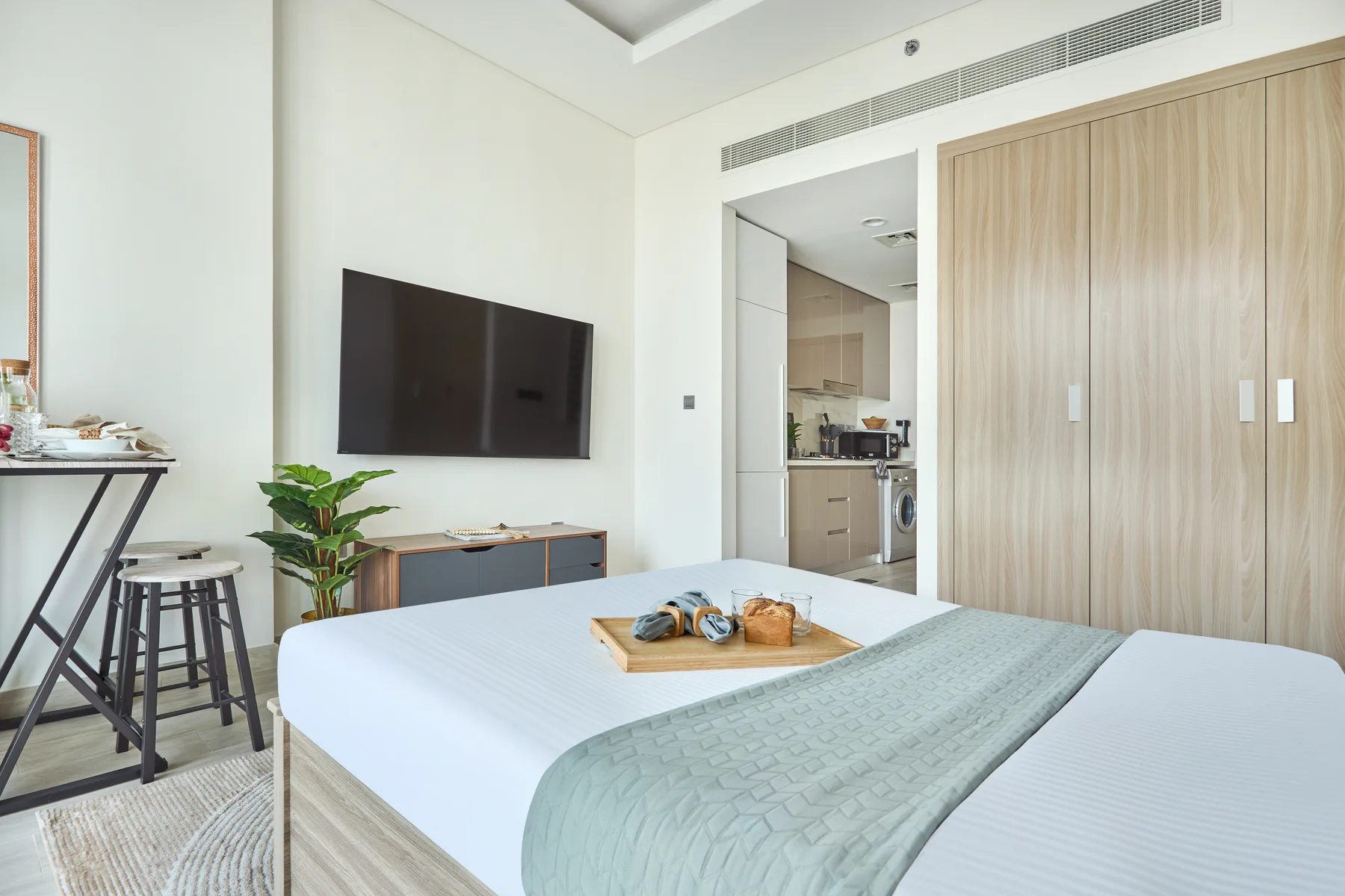 Un dormitorio luminoso con una cama bien tendida y un televisor en la pared.