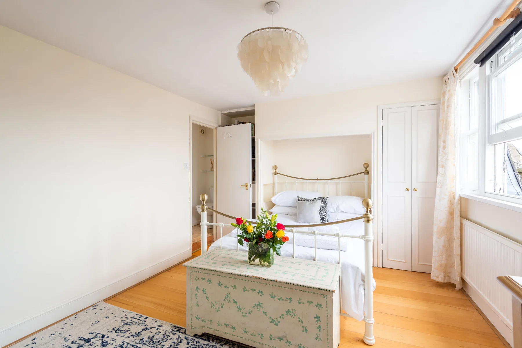 A bright bedroom with a floral chest at the foot of the bed.