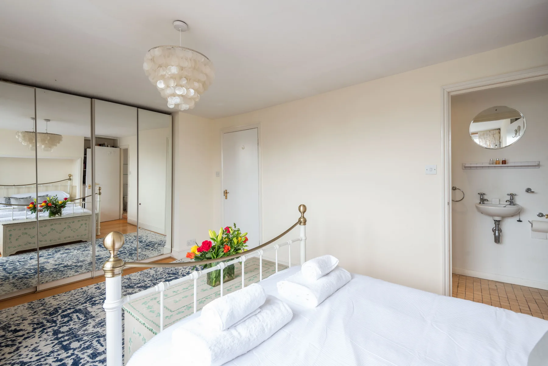 A bright bedroom with a white bed and mirrored wardrobe doors.