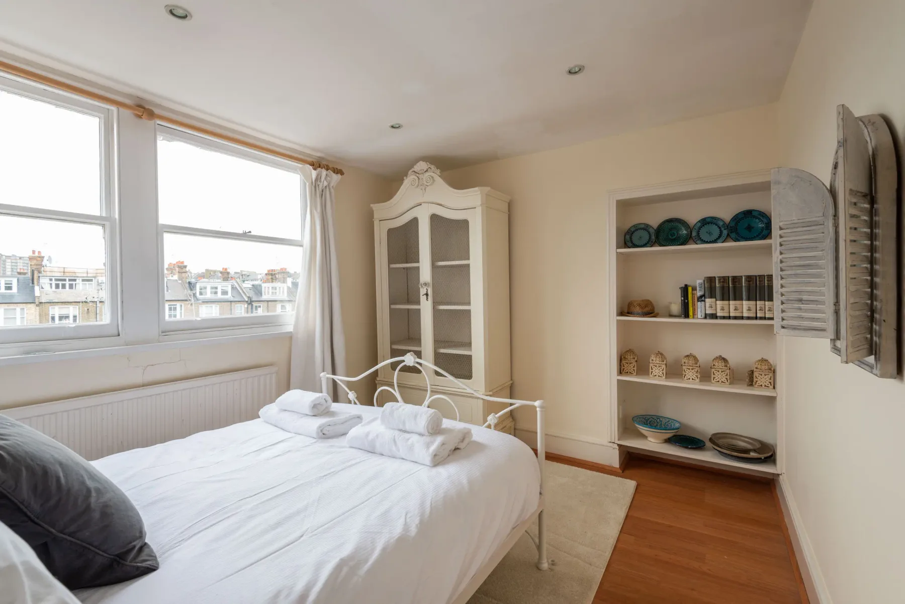 A bright bedroom with a bed, large windows, and built-in shelving.