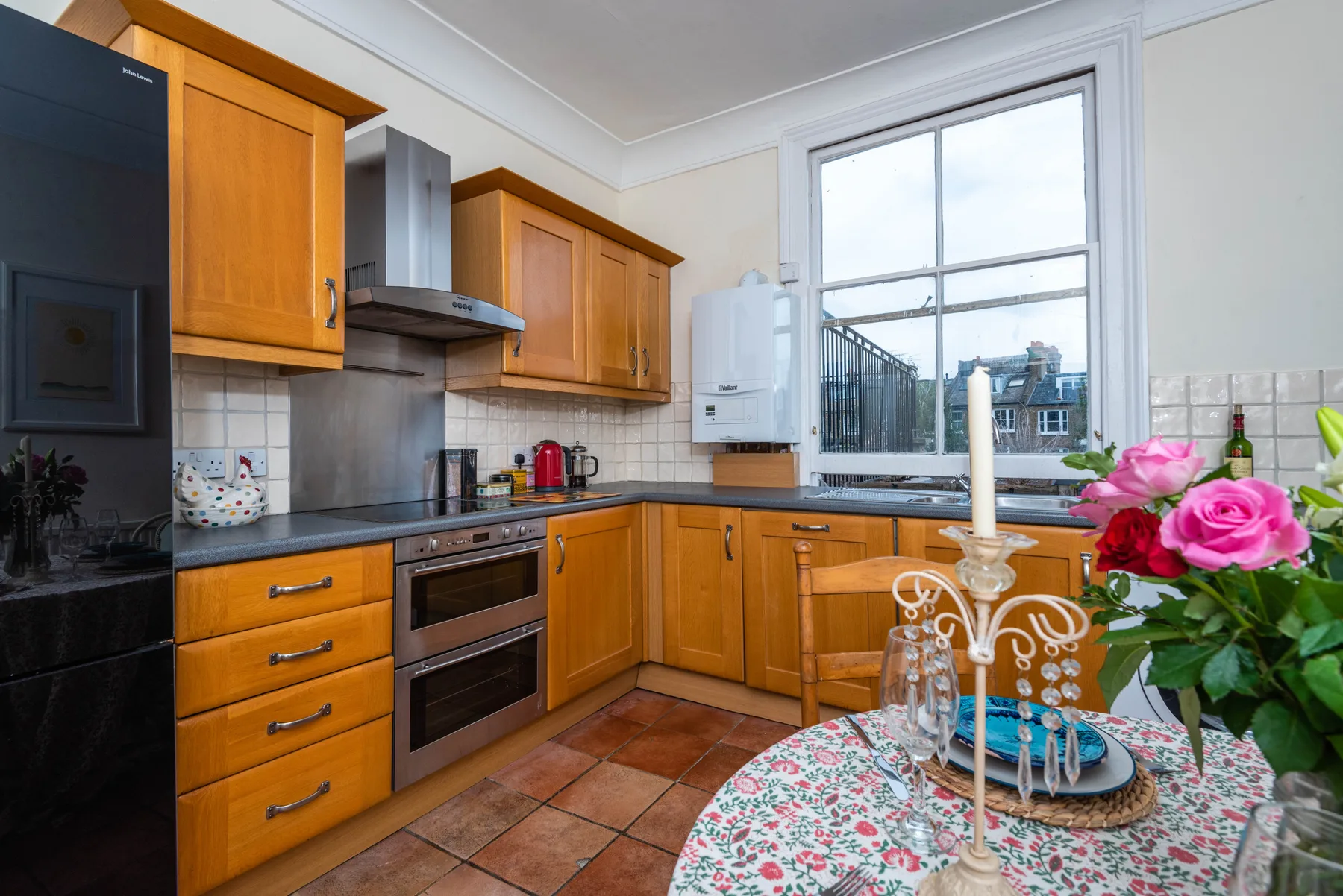 A bright kitchen with wooden cabinets and a dining table set with flowers.