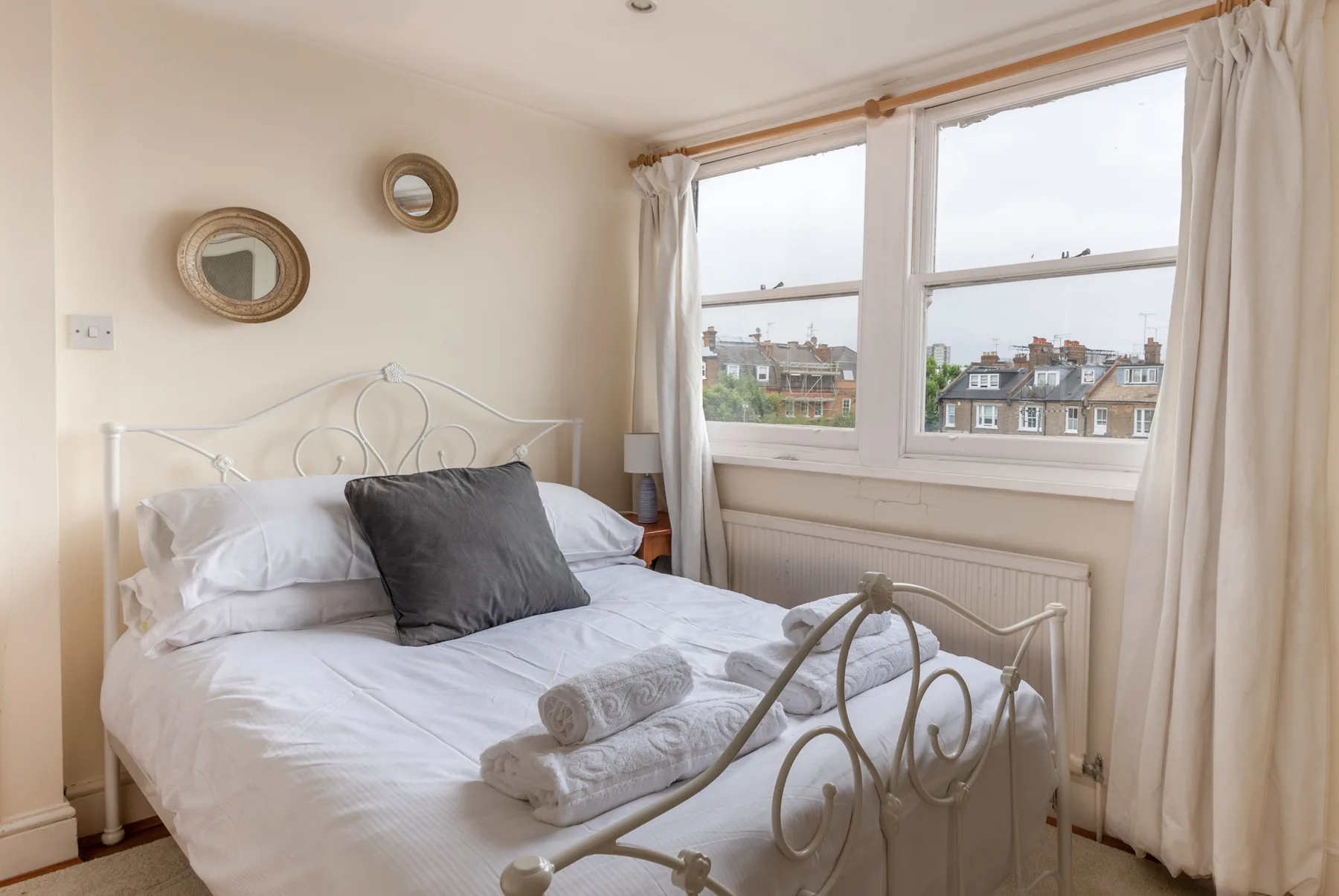 A bright bedroom with a neatly made bed beside large windows.