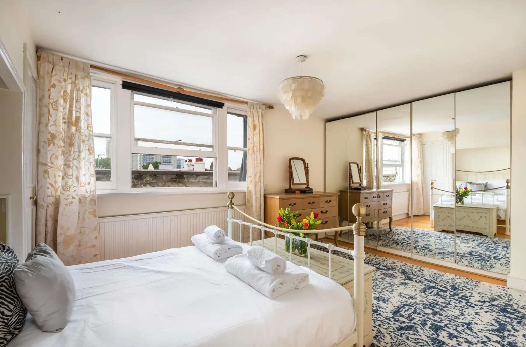 A bright bedroom with a bed, large windows, and mirrored wardrobes.