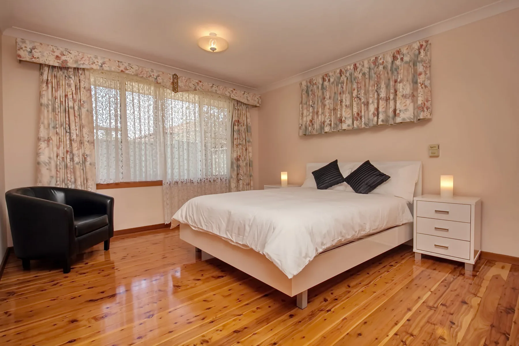 Dormitorio con una cama, un sillón negro y cortinas florales.