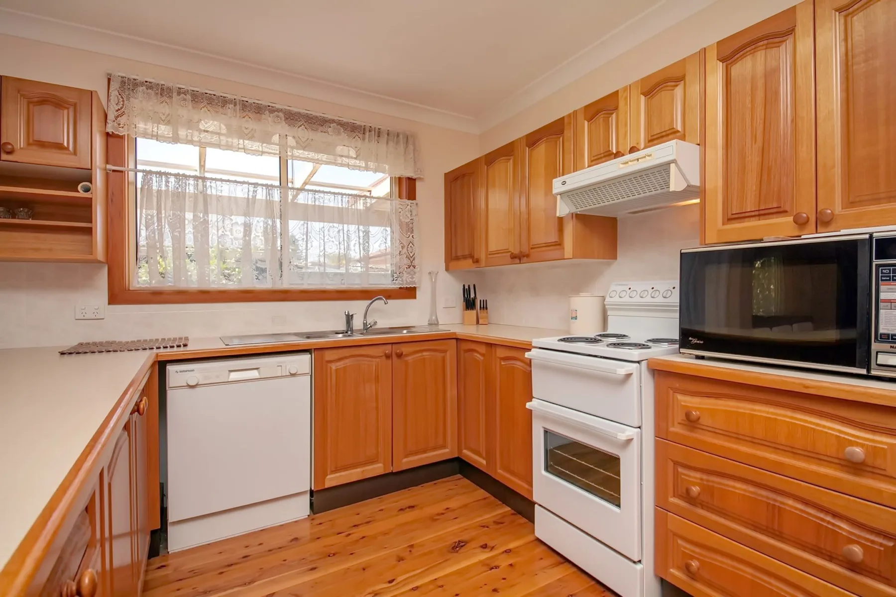 Una cocina con gabinetes de madera, una ventana y electrodomésticos blancos.
