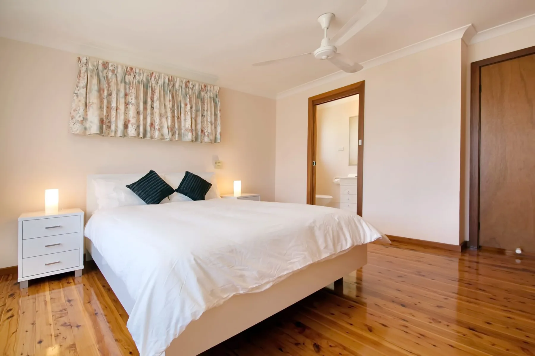 Dormitorio con una cama blanca, una mesita de noche y suelo de madera.