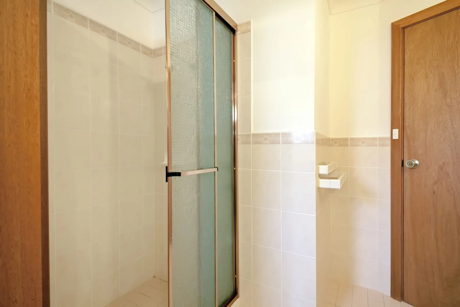 Baño con azulejos, ducha de vidrio y puerta de madera.
