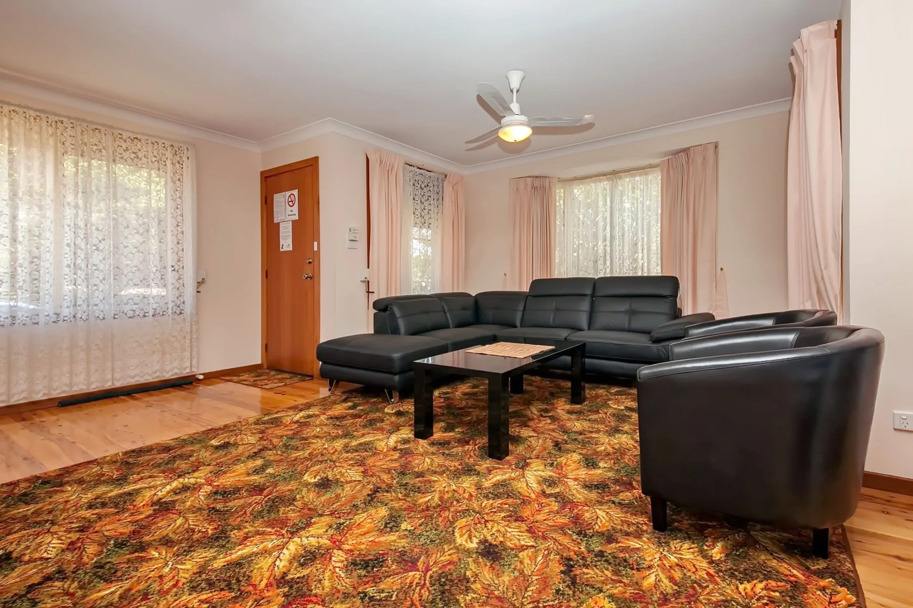 Una sala de estar con asientos oscuros, una mesa de centro y ventanas con cortinas.