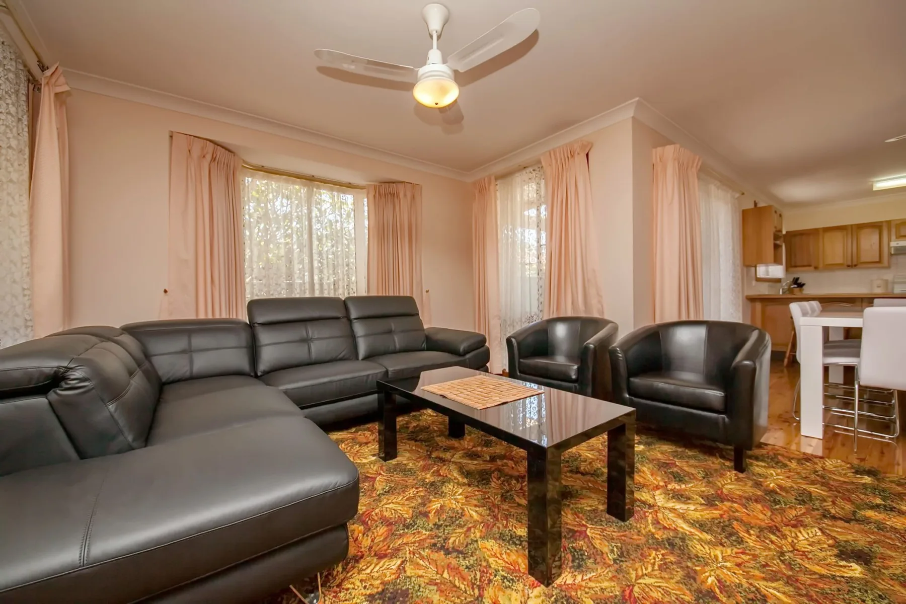 Una sala de estar con asientos oscuros, una mesa de centro y ventanas con cortinas.