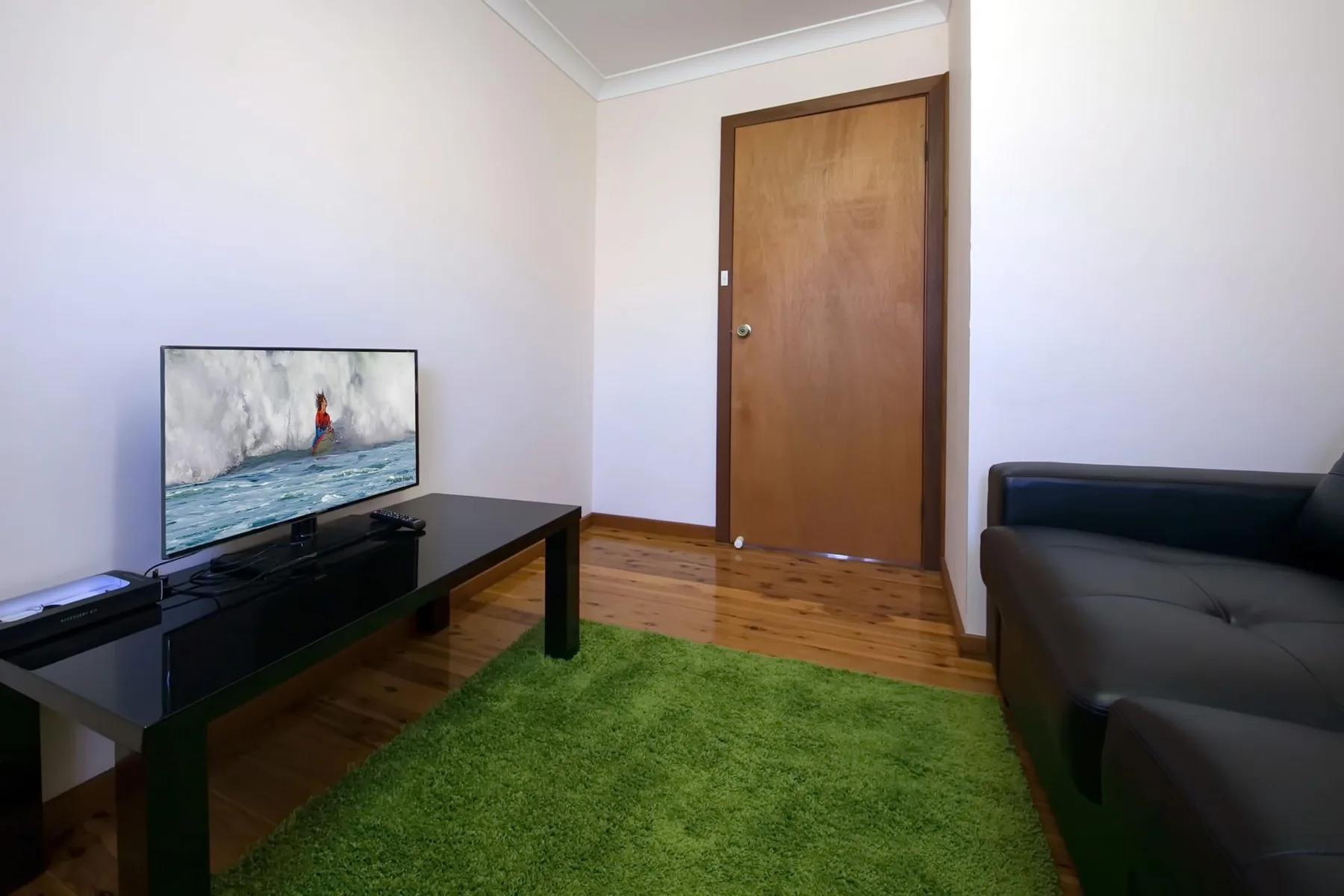 Una sala de estar con un televisor, asientos oscuros y una alfombra verde.