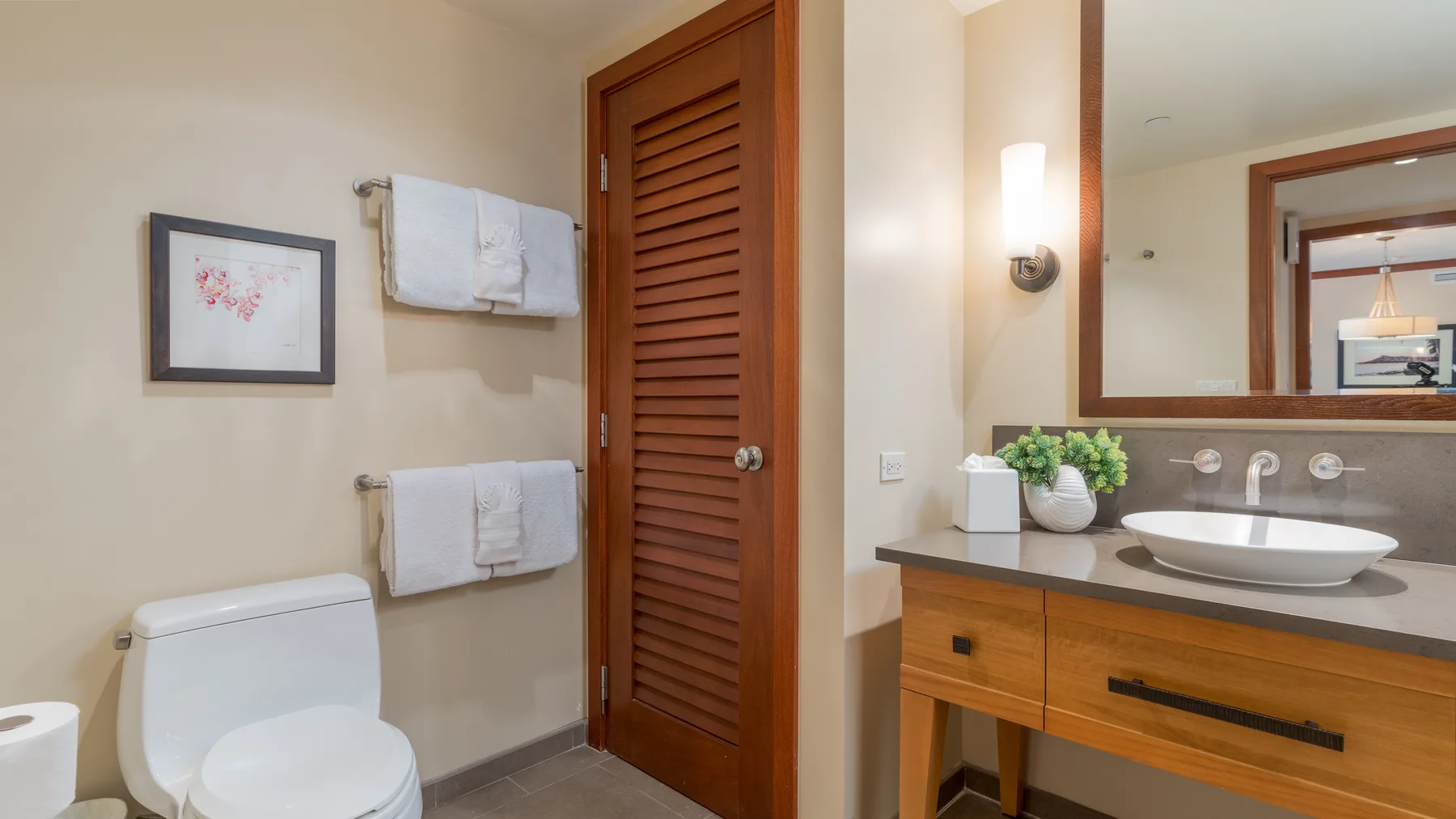 Un tocador de baño con lavabo y espejo está junto al inodoro y a los toalleros.