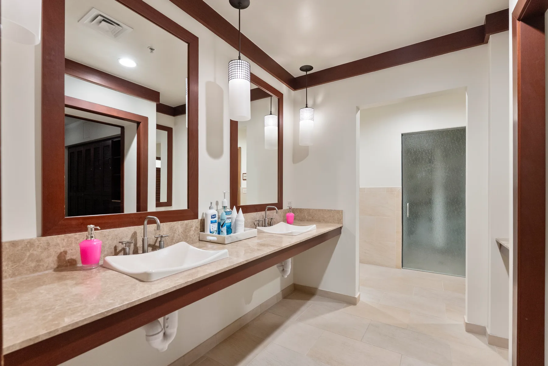 Un tocador de baño con lavabos y espejos junto a una ducha de vidrio.