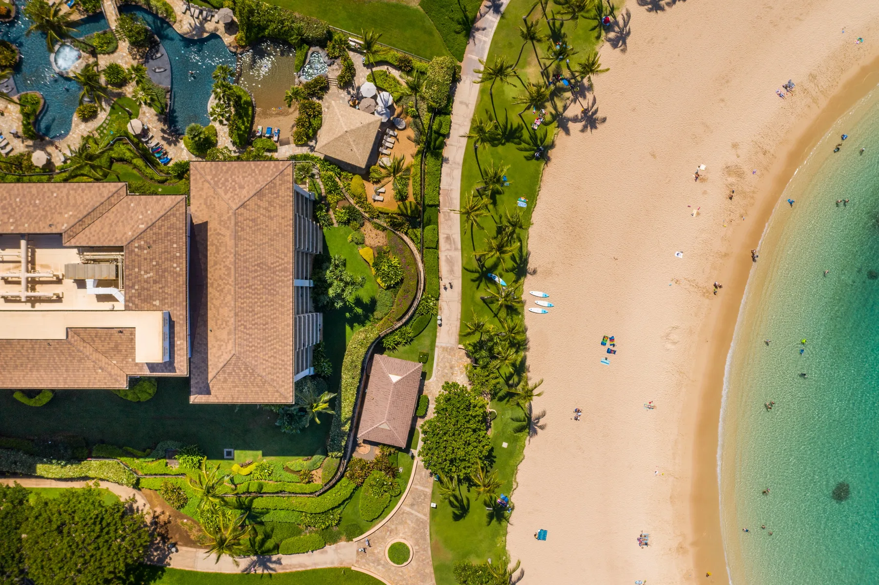 Vista aérea de un complejo turístico junto a la playa, con arena y jardines.