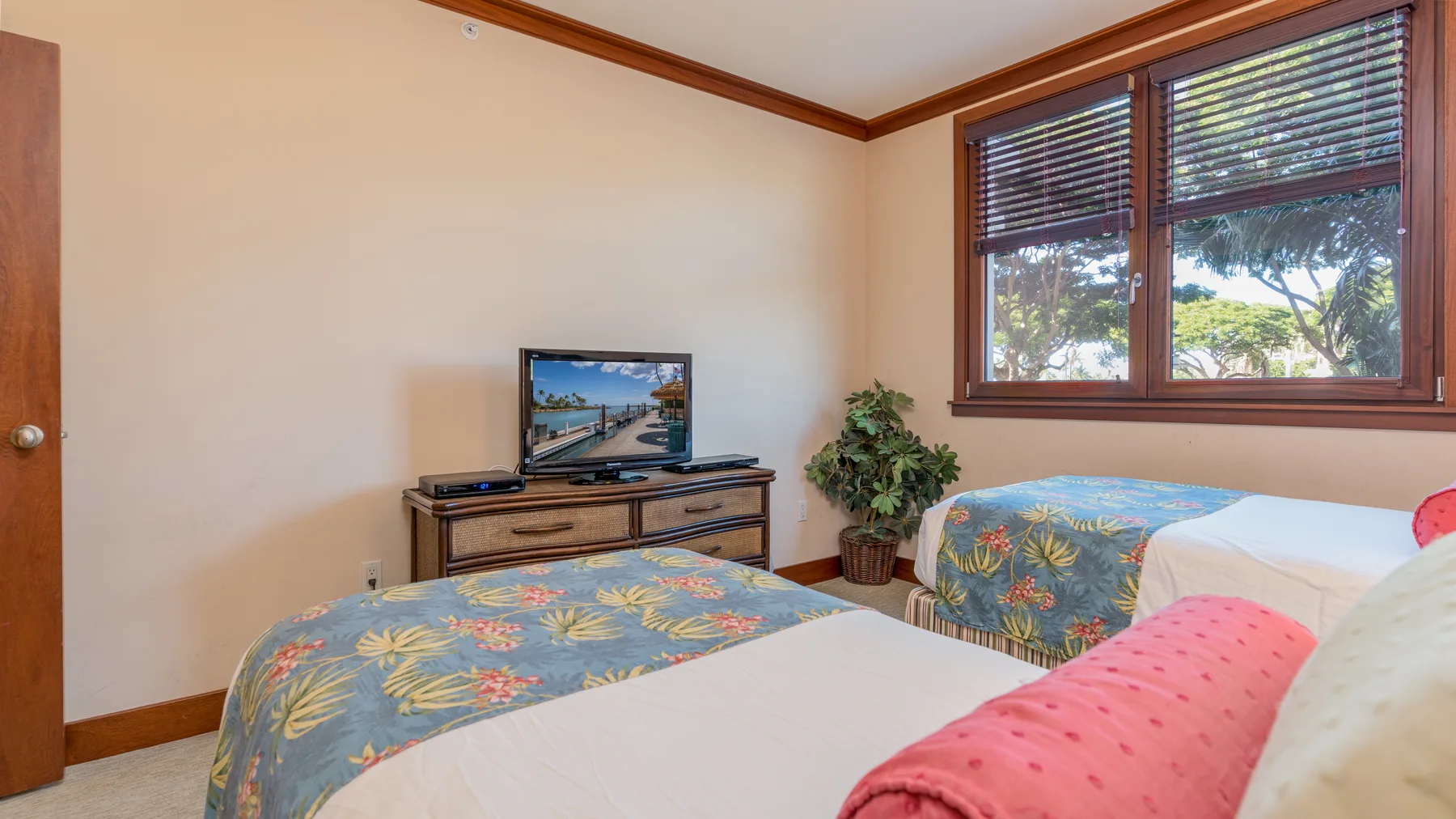 Dormitorio con dos camas, un televisor y una ventana con vista a los árboles.