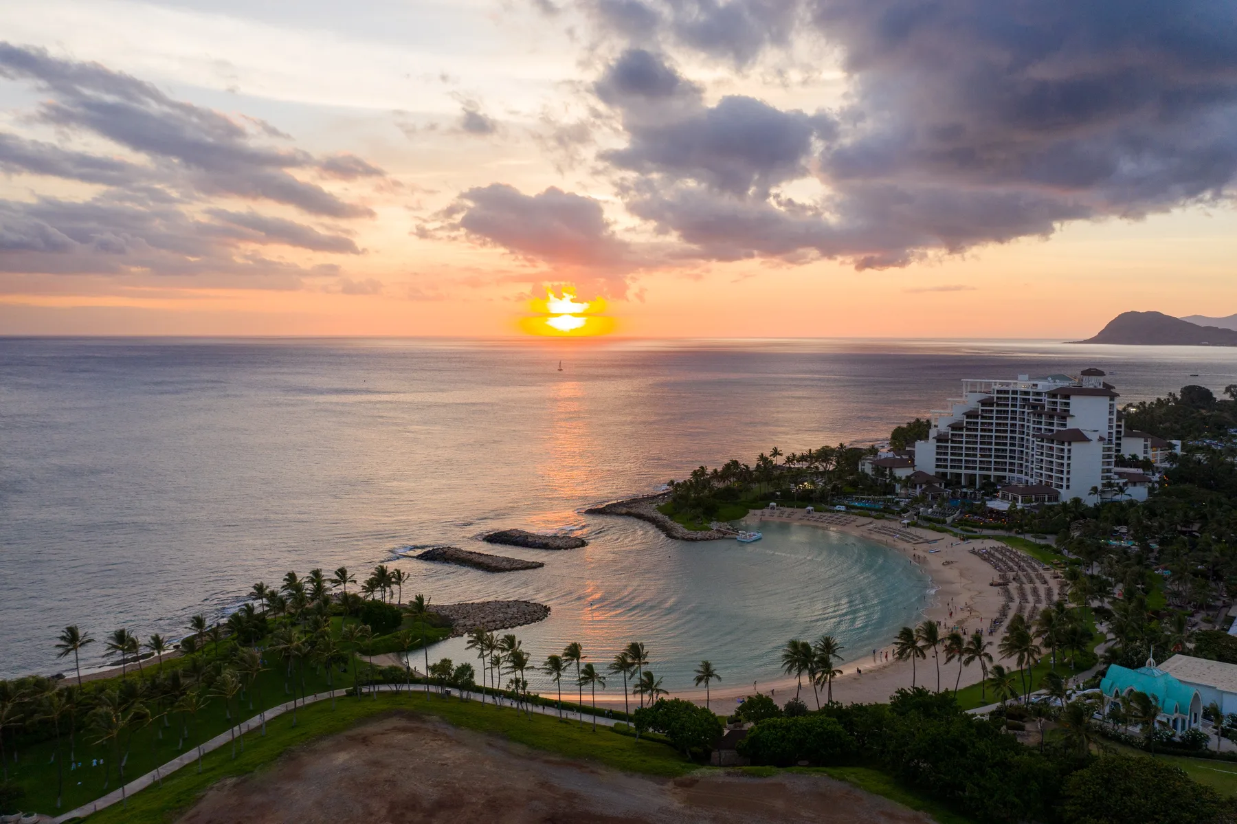 Vista aérea de una playa curva y edificios costeros al atardecer.