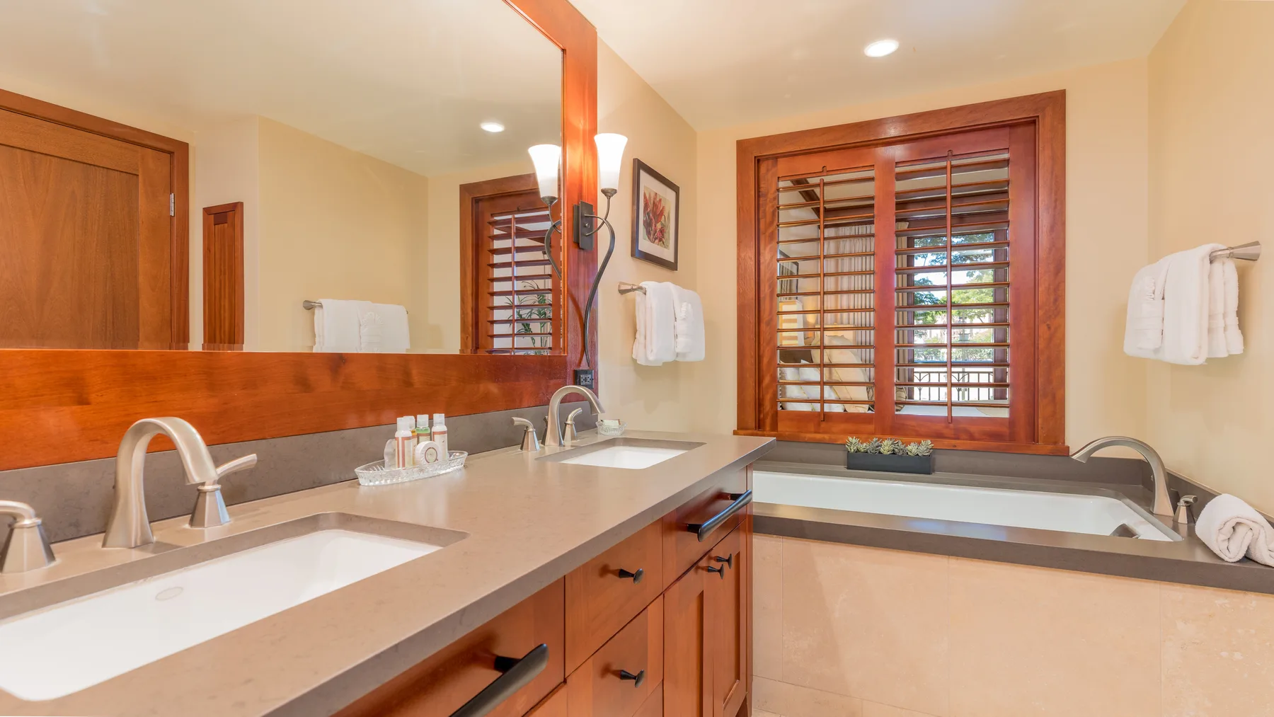 Un lavabo de baño con un espejo amplio y una ventana con persianas de madera.