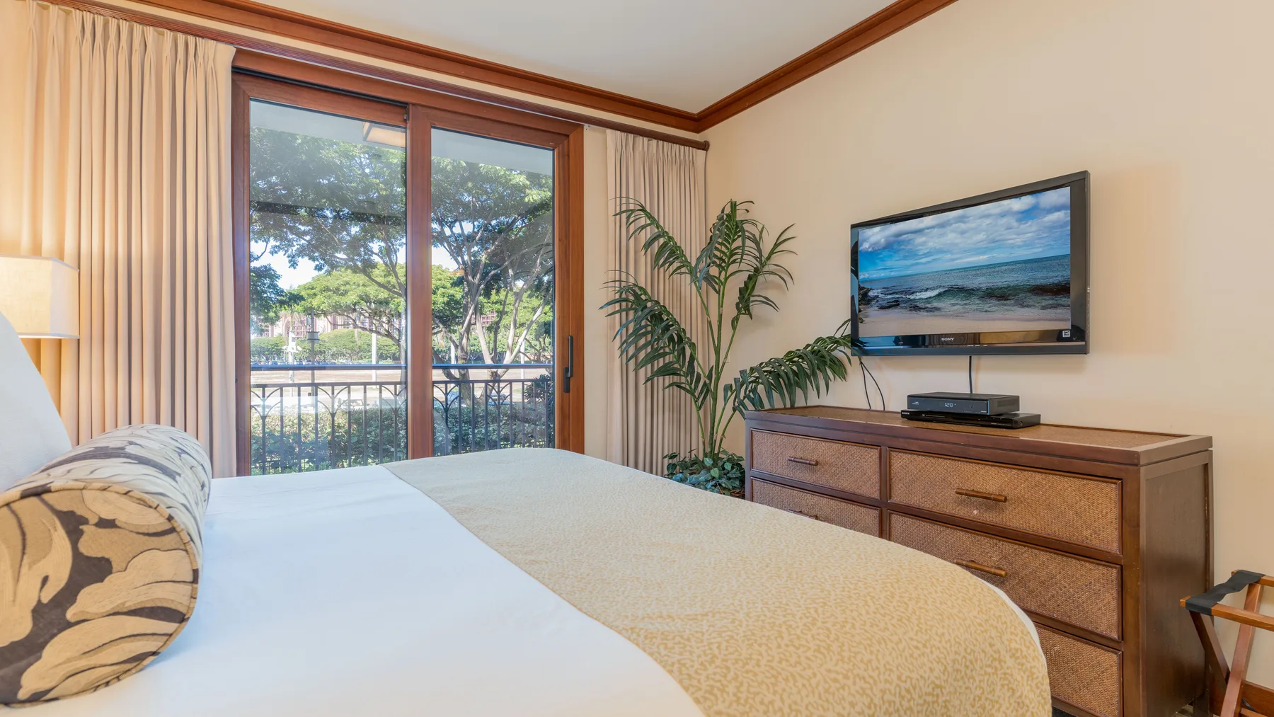 Un dormitorio con una cama, una cómoda y un televisor junto a una puerta corrediza de vidrio.