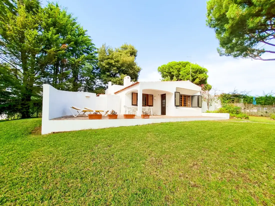 Una casa blanca se alza junto a un césped verde y árboles frondosos.