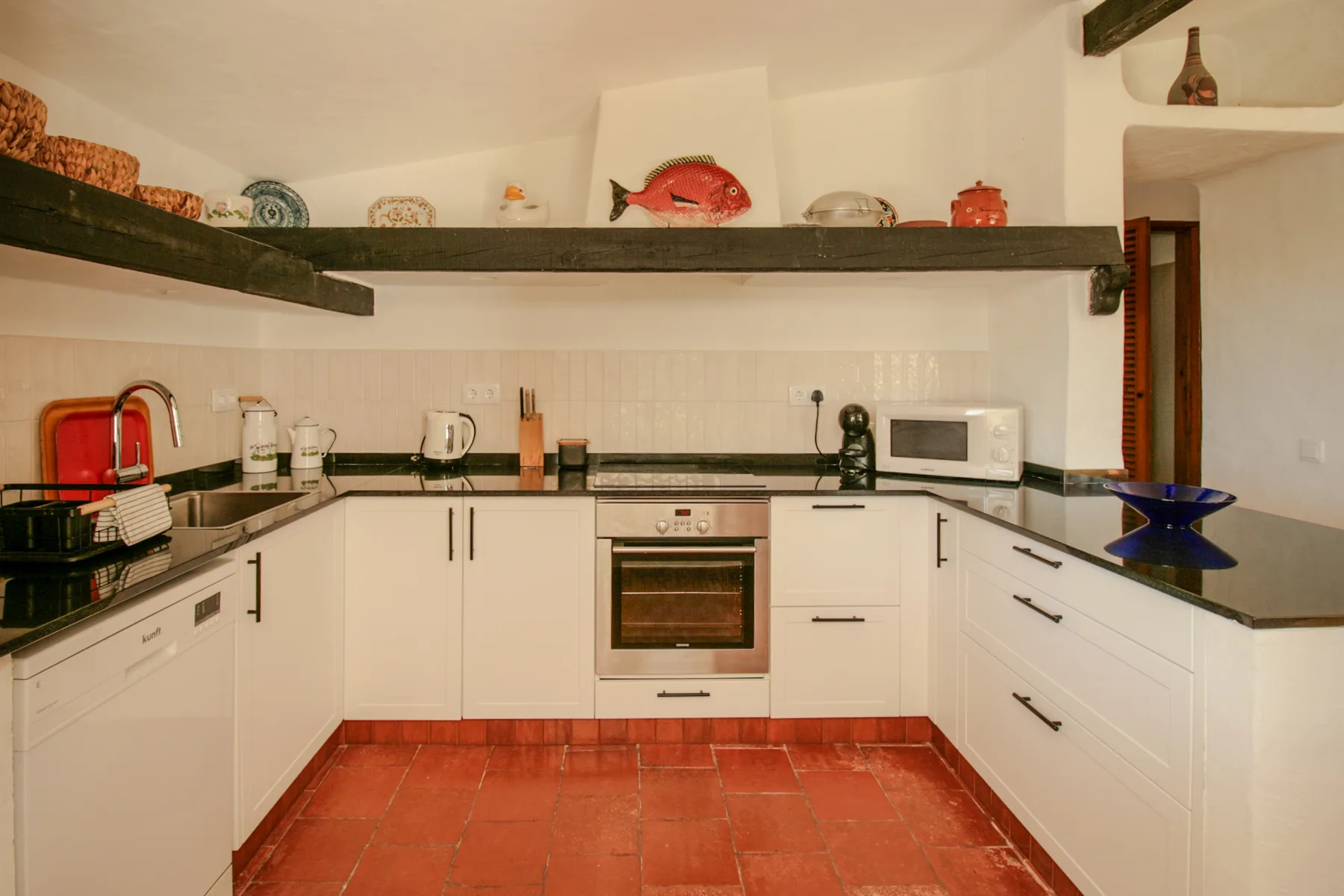 Una cocina luminosa con armarios blancos, encimeras y un horno empotrado.