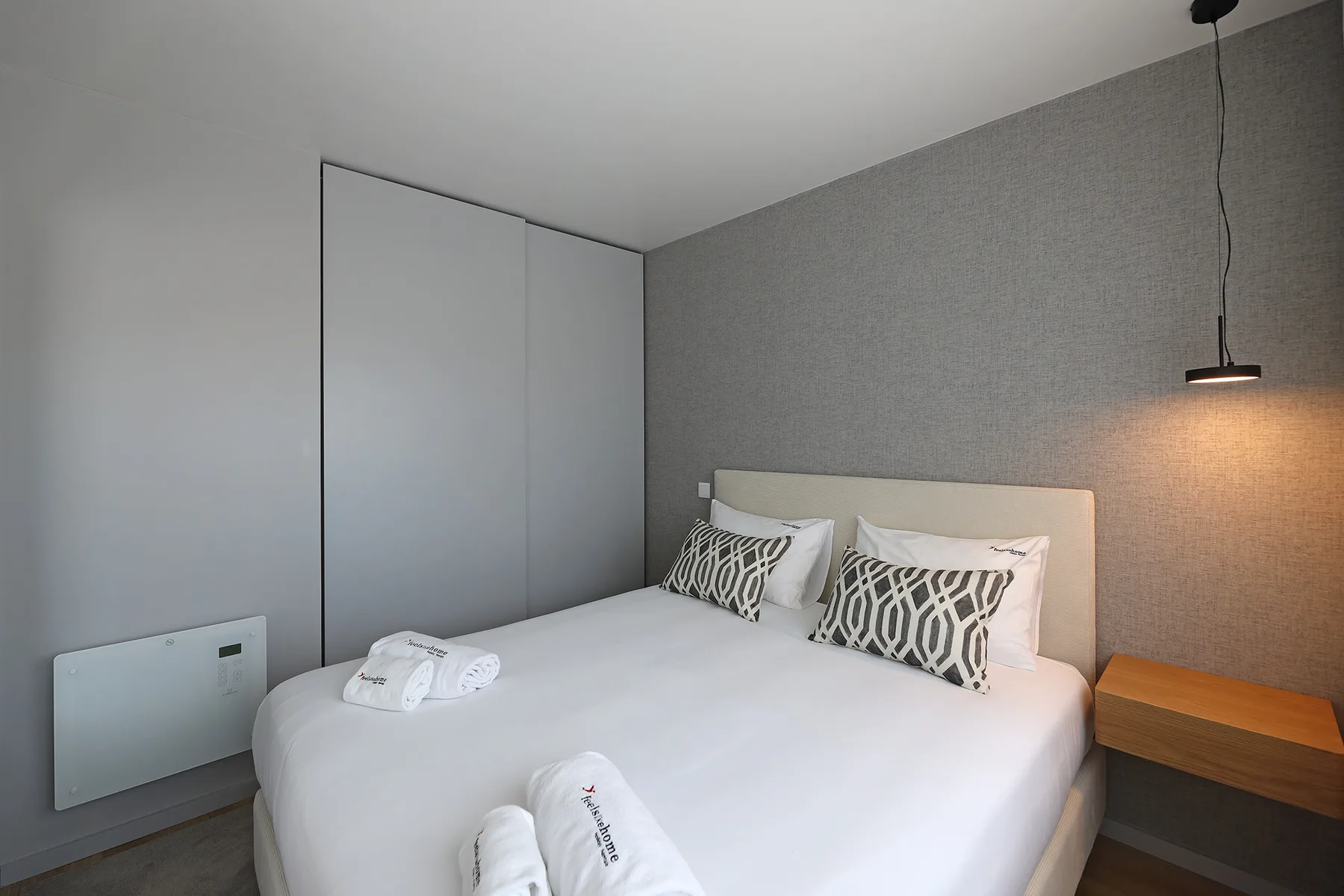 A bedroom with a neatly made bed and a pendant light.