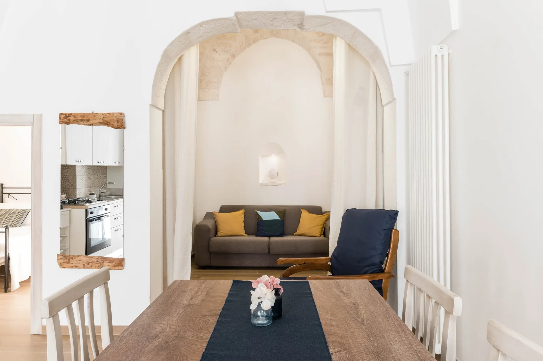 A bright living and dining area has a table, seating, and an arched alcove.