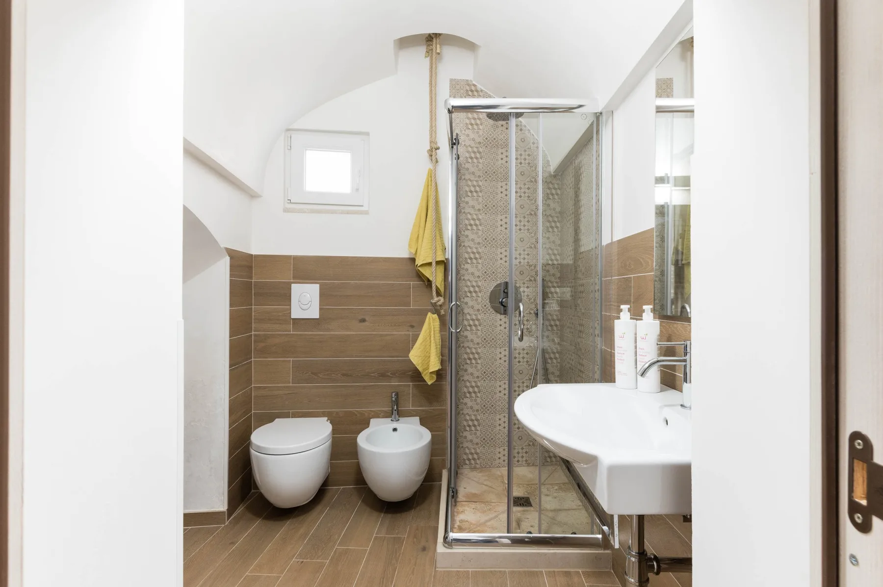 A bathroom with a glass shower, sink, and brown tiled walls.