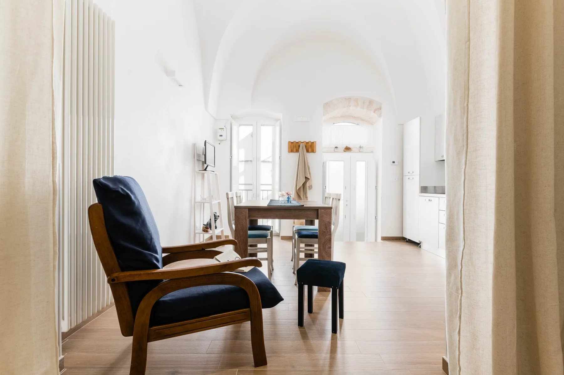 A bright dining and sitting area has a wooden table, dark seating, and tall arched ceilings.