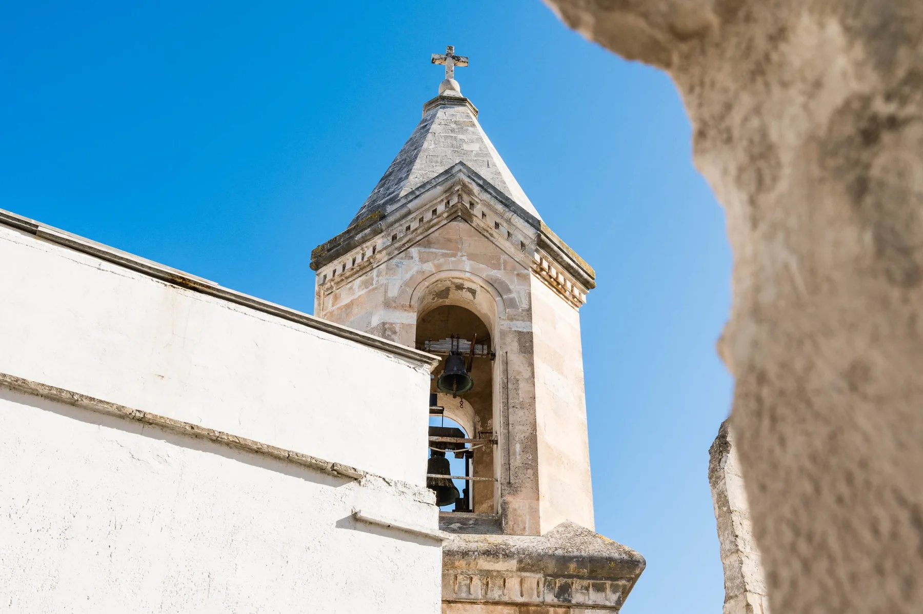 A stone bell tower rises above a white building against a clear blue sky.