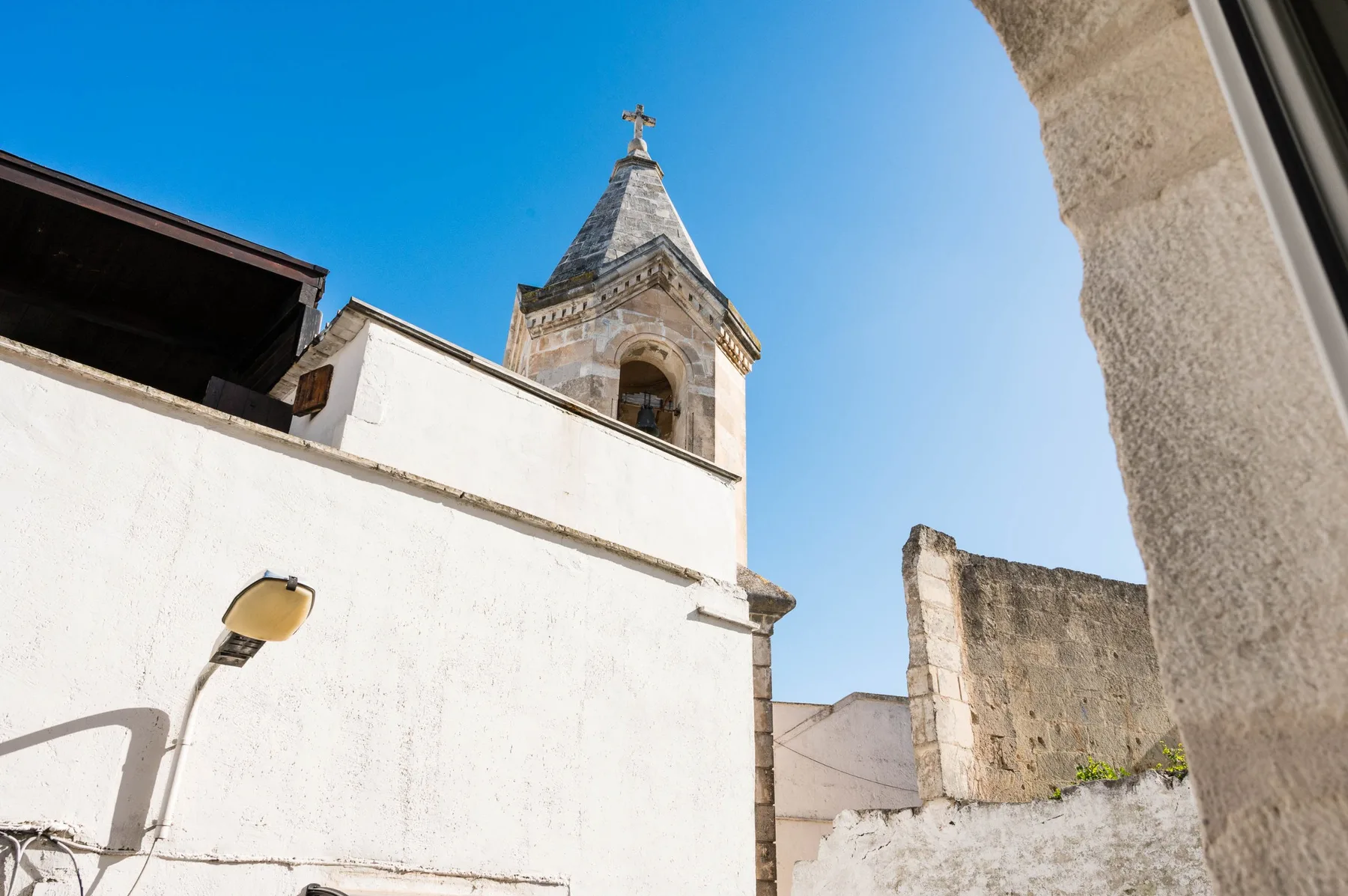A stone bell tower rises above white walls beneath a clear blue sky.